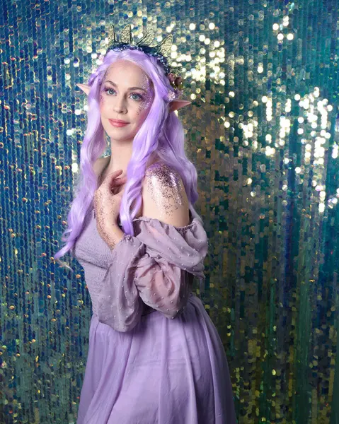 portrait of cute female model with long purple hair wearing a fantasy fairy flower crown with elf ears. Isolated on sparkling rainbow sequin background with glitter.