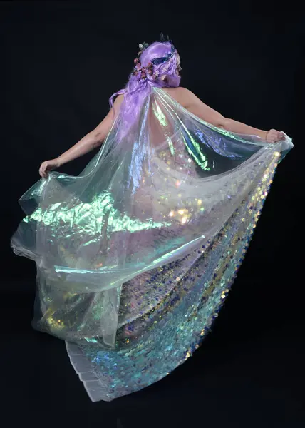 stock image Full length portrait of beautiful female model with long purple hair wearing elf ears, a fantasy fairy crown and  rainbow glitter sequin ball gown.  walking away, back view, isolated dark studio 