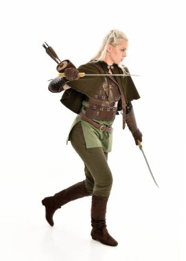 Sarışın kadın modelin yeşil fantezi elf savaşçı cadılar bayramı kostümü giymiş deri zırhlı portresi. Ayakta durarak, silah tutarak. Beyaz stüdyo arka planında izole.