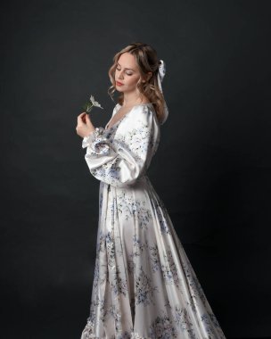 Güzel sarışın kadın modelin portresi. Çiçek desenli, romantik, tarihsel ipekten bir elbise giyiyor. Seçkin duruş, karanlık stüdyo arka planında izole edilmiş..