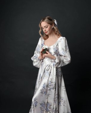 Güzel sarışın kadın modelin portresi. Çiçek desenli, romantik, tarihsel ipekten bir elbise giyiyor. Seçkin duruş, karanlık stüdyo arka planında izole edilmiş..