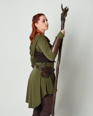  portrait of beautiful red haired female model, wearing green medieval fantasy costume with brown tunic armour armour. Standing pose with wood wizard staff weapon, isolated white studio background. clipart