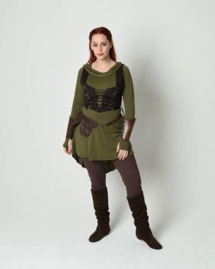 Yeşil ortaçağ fantezi deri zırh giyen kızıl saçlı kadın modelin tam boy portresi, dramatik uzun kadife kapüşonlu pelerin. Yürüyen poz, izole edilmiş beyaz stüdyo arka planı..