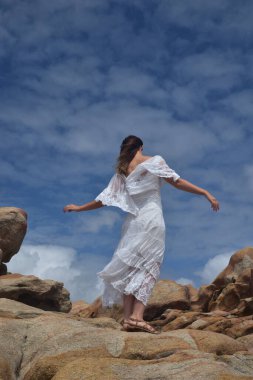 Beyaz tanrıça elbisesi giymiş kadın modelin portresi kayalık okyanus kıyısının kayalık uçurumlarla çevrili dramatik doğal manzarası. Castle Rock, Busselton, Batı Avustralya