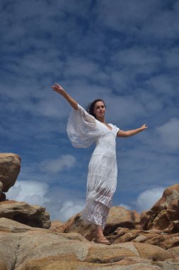 Beyaz tanrıça elbisesi giymiş kadın modelin portresi kayalık okyanus kıyısının kayalık uçurumlarla çevrili dramatik doğal manzarası. Castle Rock, Busselton, Batı Avustralya