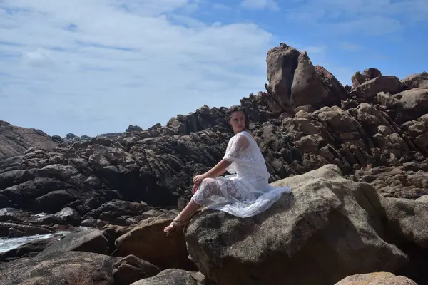 Beyaz tanrıça elbisesi giymiş kadın modelin portresi kayalık okyanus kıyısının kayalık uçurumlarla çevrili dramatik doğal manzarası. Castle Rock, Busselton, Batı Avustralya