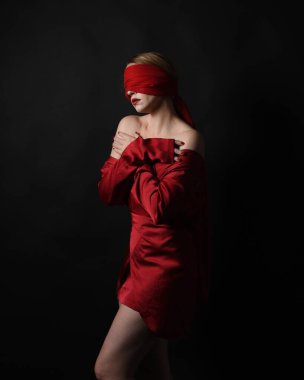 Kırmızı ipek elbise giyen ve gözlerini bağlayan kumaştan bir kadın manken portresi. Karanlık bir stüdyonun arka planında karamsar duygusal kol hareketleriyle izole edilmiş..