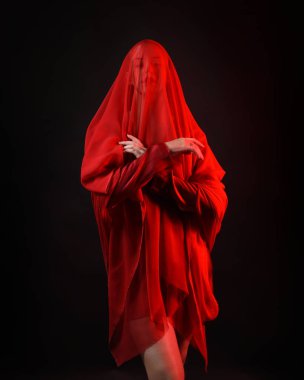 Dramatik bir portre. Kırmızı kumaş peçe takan, karamsar duygusal hareketleriyle karanlık bir stüdyo arka planında izole edilmiş hayalet bir kadın model..