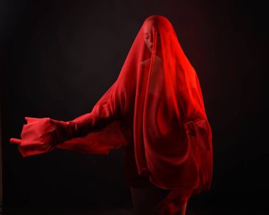 Dramatik bir portre. Kırmızı kumaş peçe takan, karamsar duygusal hareketleriyle karanlık bir stüdyo arka planında izole edilmiş hayalet bir kadın model..
