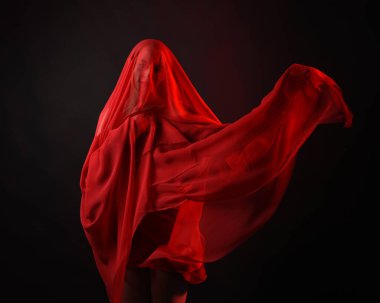 Dramatik bir portre. Kırmızı kumaş peçe takan, karamsar duygusal hareketleriyle karanlık bir stüdyo arka planında izole edilmiş hayalet bir kadın model..