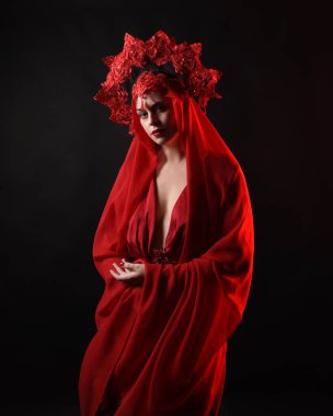 Dramatik yakın plan portre kırmızı ipek elbise giyen bir kadın model ve peçeli muhteşem bir fantezi taç. Karanlık bir stüdyonun arka planında karamsar duygusal kol hareketleriyle izole edilmiş..