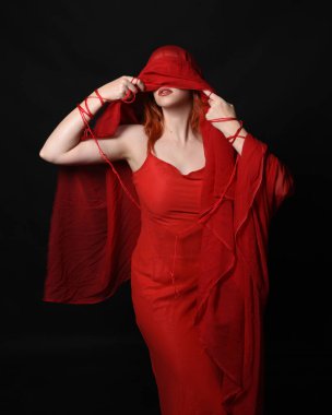 Göz bağı ve kırmızı elbise gibi başörtüsü takan güzel bir kadın modelin portresi. Kollara dolanmış düğümlü ip, birbirine dolanmış halat tutan eller. Karanlık stüdyo arka planında izole.