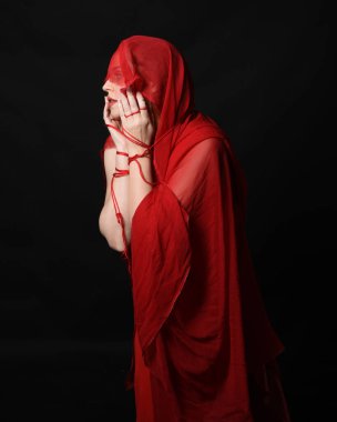 Göz bağı ve kırmızı elbise gibi başörtüsü takan güzel bir kadın modelin portresi. Kollara dolanmış düğümlü ip, birbirine dolanmış halat tutan eller. Karanlık stüdyo arka planında izole.