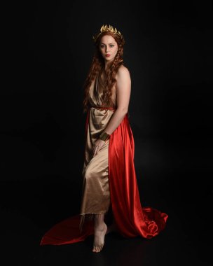 Yunan kırmızı ipek Roma cübbesi giyen güzel bir kadın modelin tam boy portresi, taç takan tarihi fantezi tanrıçası kostümü. Karanlık stüdyo arka planında yalnız poz vermek.