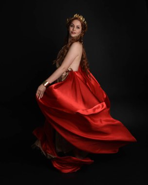 Yunan kırmızı ipek Roma cübbesi giyen güzel bir kadın modelin tam boy portresi, taç takan tarihi fantezi tanrıçası kostümü. Karanlık stüdyo arka planında yalnız poz vermek.