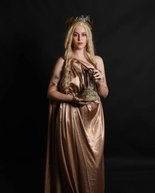 Altın sarısı ipek toga cübbe ve taç giyen güzel sarışın kadın modelin yakın plan portresi. Tarihi fantezi tanrıçası persephone elinde nar meyvesi tutuyor. Karanlık stüdyo arka planında izole.