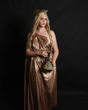 Altın sarısı ipek toga cübbe ve taç giyen güzel sarışın kadın modelin yakın plan portresi. Tarihi fantezi tanrıçası persephone elinde nar meyvesi tutuyor. Karanlık stüdyo arka planında izole.