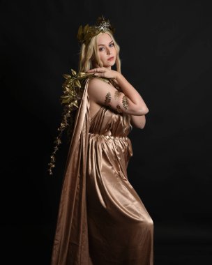 Altın sarısı ipek toga cübbe ve taç giyen güzel sarışın kadın modelin yakın plan portresi. Tarihi fantezi tanrıçası persephone elinde nar meyvesi tutuyor. Karanlık stüdyo arka planında izole.