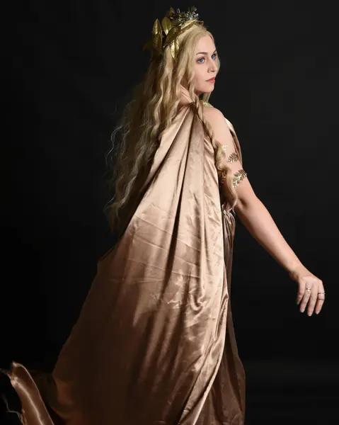 stock image Close up portrait of beautiful blonde female model wearing gold grecian silk toga robes and crown, historical fantasy goddess persephone holding pomegranate fruit. isolated on dark studio background.