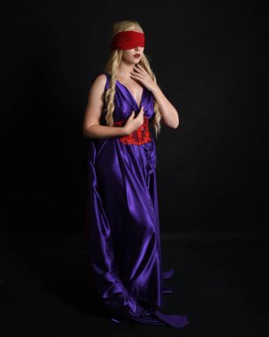 Close up portrait of beautiful blonde female model wearing silk grecian toga dress and red blindfold, historical fantasy goddess,  isolated on dark studio background. clipart