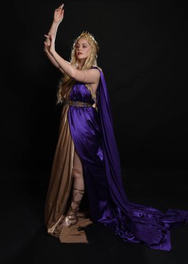 Mor ve altın renkli ipek toga cüppeli, kraliyet tacıyla, tarihi fantezi tanrıçası kostümü giymiş güzel sarışın kadın modelin tam boy portresi. Karanlık stüdyo arka planında izole edilmiş..