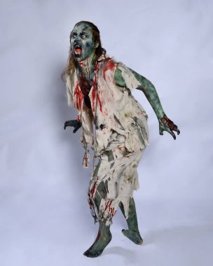 Korkunç cadılar bayramı kostümü giyen korkunç kadın modelin portresi yırtık giysiler ve sahte kan ölümsüz bir zombi karakteri gibi. Karanlık stüdyo arka planında yürüyen bir figür.