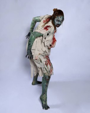 Korkunç cadılar bayramı kostümü giyen korkunç kadın modelin portresi yırtık giysiler ve sahte kan ölümsüz bir zombi karakteri gibi. Karanlık stüdyo arka planında yürüyen bir figür.