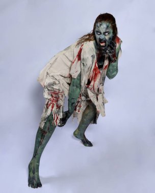 Korkunç cadılar bayramı kostümü giyen korkunç kadın modelin portresi yırtık giysiler ve sahte kan ölümsüz bir zombi karakteri gibi. Karanlık stüdyo arka planında yürüyen bir figür.