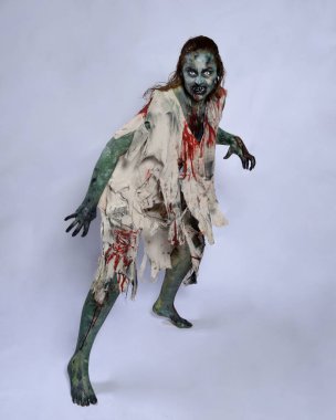 Korkunç cadılar bayramı kostümü giyen korkunç kadın modelin portresi yırtık giysiler ve sahte kan ölümsüz bir zombi karakteri gibi. Karanlık stüdyo arka planında yürüyen bir figür.