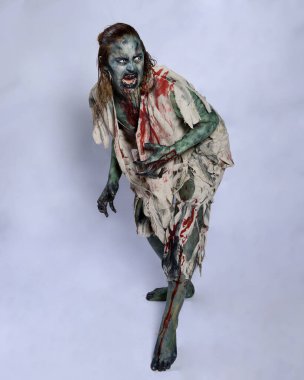Korkunç cadılar bayramı kostümü giyen korkunç kadın modelin portresi yırtık giysiler ve sahte kan ölümsüz bir zombi karakteri gibi. Karanlık stüdyo arka planında yürüyen bir figür.