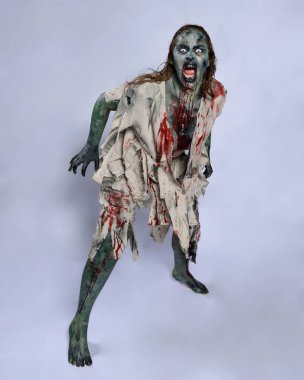 Korkunç cadılar bayramı kostümü giyen korkunç kadın modelin portresi yırtık giysiler ve sahte kan ölümsüz bir zombi karakteri gibi. Karanlık stüdyo arka planında yürüyen bir figür.