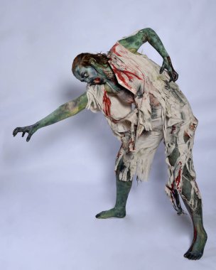 Korkunç cadılar bayramı kostümü giyen korkunç kadın modelin portresi yırtık giysiler ve sahte kan ölümsüz bir zombi karakteri gibi. Karanlık stüdyo arka planında yürüyen bir figür.