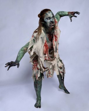 Korkunç cadılar bayramı kostümü giyen korkunç kadın modelin portresi yırtık giysiler ve sahte kan ölümsüz bir zombi karakteri gibi. Karanlık stüdyo arka planında yürüyen bir figür.