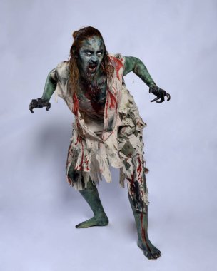 Korkunç cadılar bayramı kostümü giyen korkunç kadın modelin portresi yırtık giysiler ve sahte kan ölümsüz bir zombi karakteri gibi. Karanlık stüdyo arka planında yürüyen bir figür.