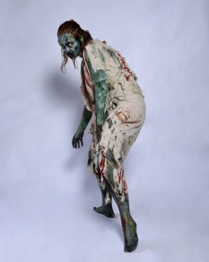 Korkunç cadılar bayramı kostümü giyen korkunç kadın modelin portresi yırtık giysiler ve sahte kan ölümsüz bir zombi karakteri gibi. Karanlık stüdyo arka planında yürüyen bir figür.