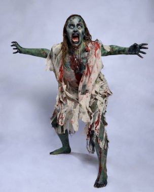 Korkunç cadılar bayramı kostümü giyen korkunç kadın modelin portresi yırtık giysiler ve sahte kan ölümsüz bir zombi karakteri gibi. Karanlık stüdyo arka planında yürüyen bir figür.