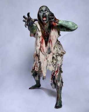 Korkunç cadılar bayramı kostümü giyen korkunç kadın modelin portresi yırtık giysiler ve sahte kan ölümsüz bir zombi karakteri gibi. Karanlık stüdyo arka planında yürüyen bir figür.