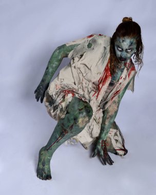 Korkunç cadılar bayramı kostümü giyen korkunç kadın modelin portresi yırtık giysiler ve sahte kan ölümsüz bir zombi karakter gibi. İzole bir figür, emekleme karanlık bir stüdyo arkaplanı oluşturuyor