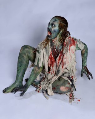 Korkunç cadılar bayramı kostümü giyen korkunç kadın modelin portresi yırtık giysiler ve sahte kan ölümsüz bir zombi karakter gibi. İzole bir figür, emekleme karanlık bir stüdyo arkaplanı oluşturuyor