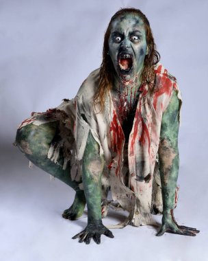 Korkunç cadılar bayramı kostümü giyen korkunç kadın modelin portresi yırtık giysiler ve sahte kan ölümsüz bir zombi karakter gibi. İzole bir figür, emekleme karanlık bir stüdyo arkaplanı oluşturuyor