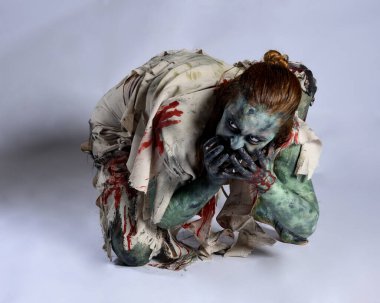 Korkunç cadılar bayramı kostümü giyen korkunç kadın modelin portresi yırtık giysiler ve sahte kan ölümsüz bir zombi karakter gibi. İzole bir figür, emekleme karanlık bir stüdyo arkaplanı oluşturuyor