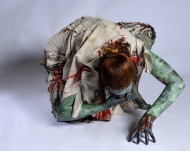 Korkunç cadılar bayramı kostümü giyen korkunç kadın modelin portresi yırtık giysiler ve sahte kan ölümsüz bir zombi karakter gibi. İzole bir figür, emekleme karanlık bir stüdyo arkaplanı oluşturuyor