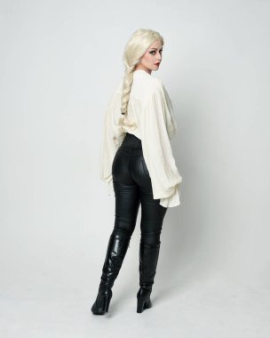  Klasik gotik fantezi bluz, siyah deri pantolon ve uzun sarı saçlar giyen kadın modelin tam boy portresi. Ayakta durmak, hareketli kollarla uzaklaşmak, beyaz stüdyo arka planında izole olmak..