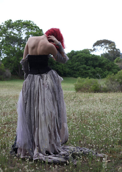 полноразмерный портрет красивой рыжеволосой женщины-модели, носящей готический сказочный костюм с порванным бальным платьем свадебного платья, черный корсет, кожаные сапоги. ходьба поза лесной пейзаж фон.