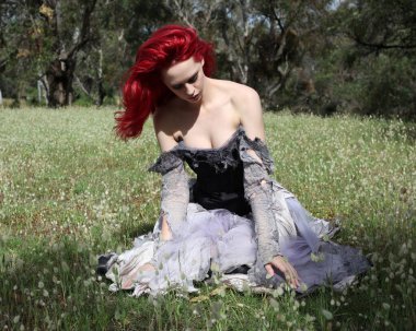 full length portrait of beautiful red haired female model figure, wearing gothic fantasy costume with torn ballgown wedding dress, black corset. sitting pose in  dreamy flower field forest scenery background. clipart