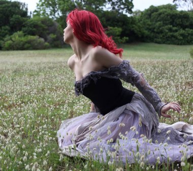 Güzel kızıl saçlı kadın modelin tam boy portresi gotik fantezi kostümlü yırtık balo elbisesi, siyah korse, deri botlar. oturma pozu orman manzarası arka planı.