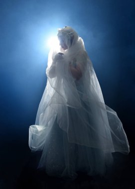 Ortaçağ masal elbisesi giymiş güzel sarışın fantezi perisi, peçeli beyaz kapüşonlu bir pelerin. dumanlı sis efektiyle izole edilmiş karanlık stüdyo arkaplanı