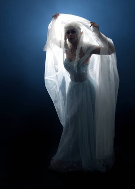 Ortaçağ masal elbisesi giymiş güzel sarışın fantezi perisi, peçeli beyaz kapüşonlu bir pelerin. dumanlı sis efektiyle izole edilmiş karanlık stüdyo arkaplanı