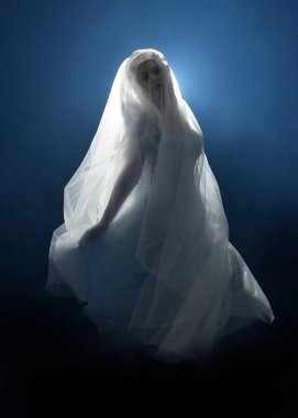 Ortaçağ masal elbisesi giymiş güzel sarışın fantezi perisi, peçeli beyaz kapüşonlu bir pelerin. dumanlı sis efektiyle izole edilmiş karanlık stüdyo arkaplanı