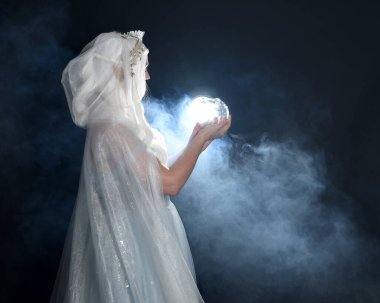 portrait beautiful blonde fantasy maiden faery wearing medieval fairytale ballgown costume, white cape and crystal crown. holding glowing crystal ball orb  isolated dark studio background with mystical smoke fog backlight lighting effect clipart